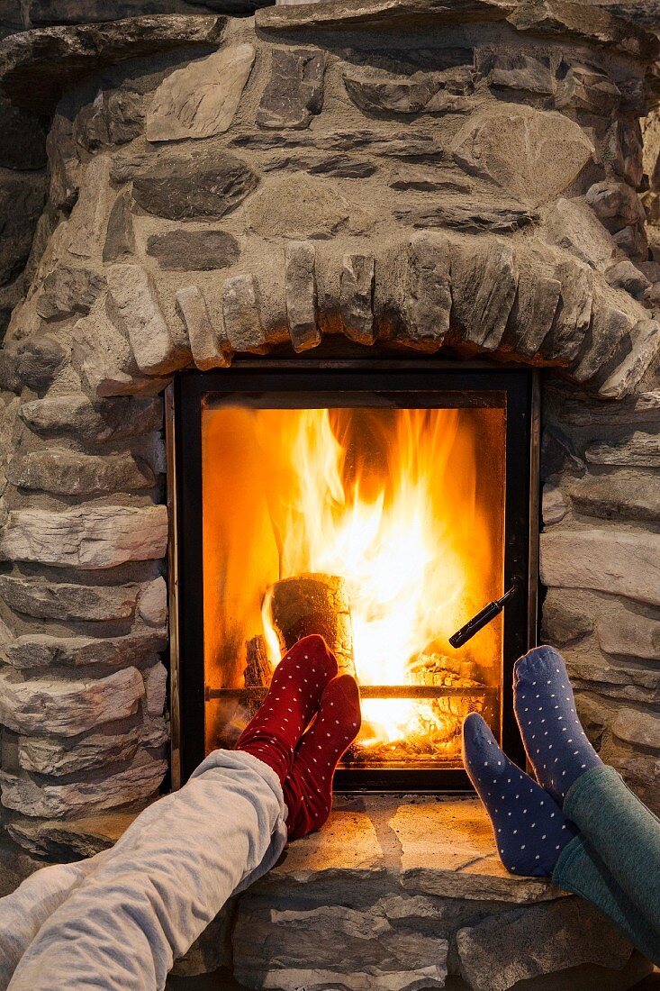 Two pairs of women's legs with red and blue socks on feet propped up in front of fireplace