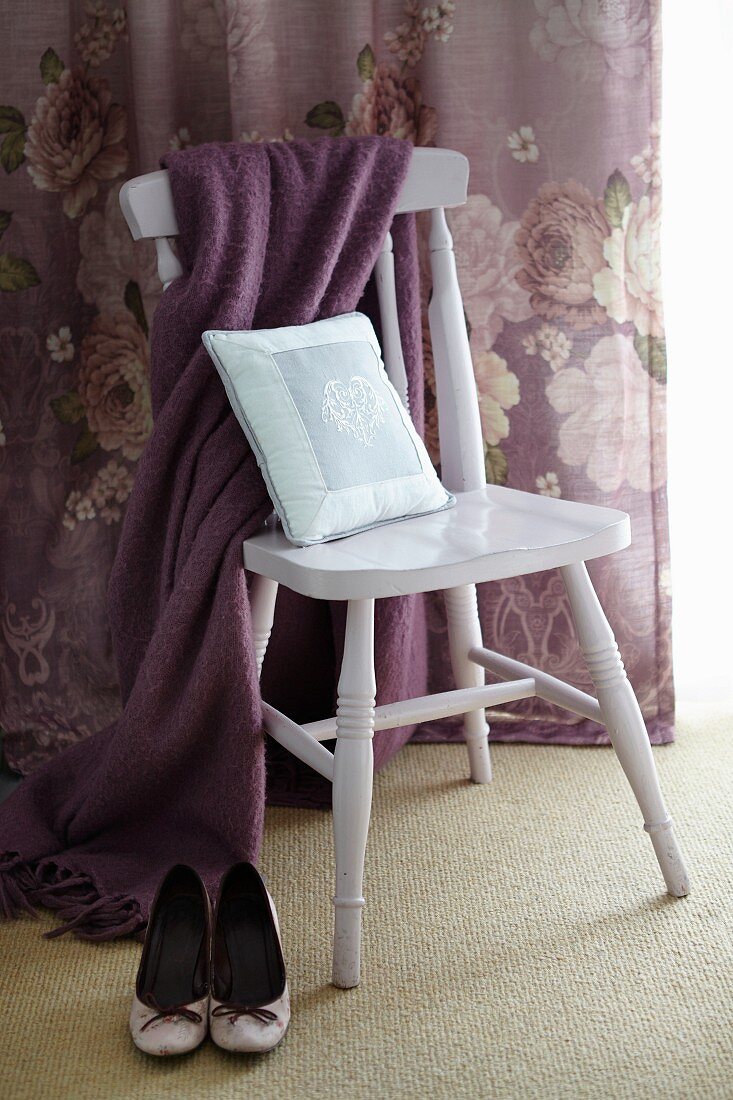High heels next to shawl and cushion on chair with floral curtain in background