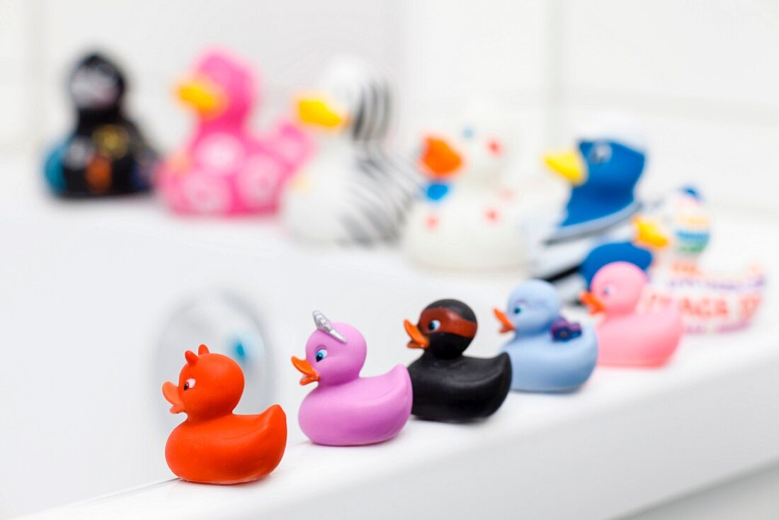 Various rubber ducks sitting on edge of bathtub