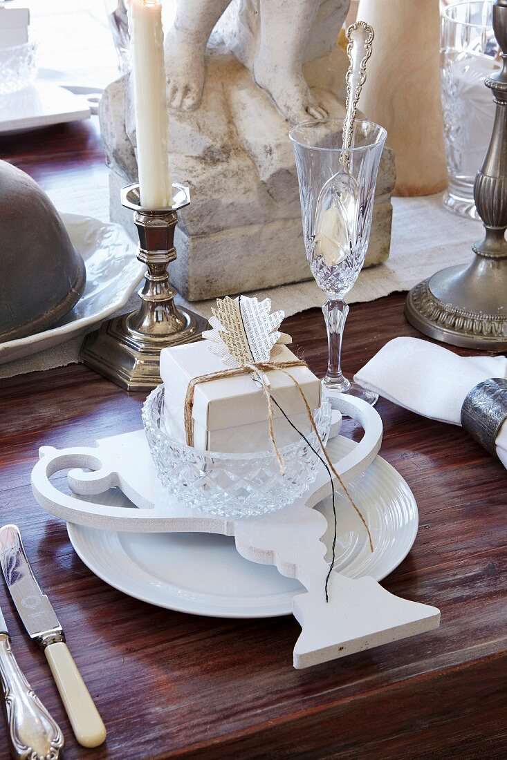 Weisses Gedeck mit nostalgischer Papierdeko, Sektglas und Silberkerzenständer auf Holztisch