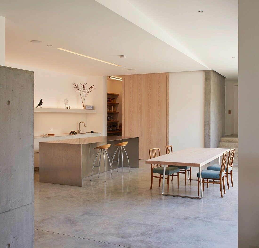Open-plan designer kitchen with island counter, dining table and upholstered chairs in minimalist interior
