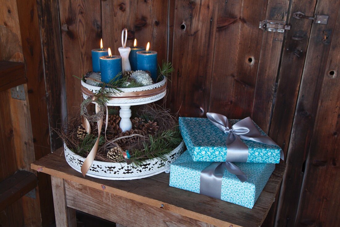 Elegant verpackte Geschenke und nostalgische Etagere mit Adventsdekoration vor Holzwand