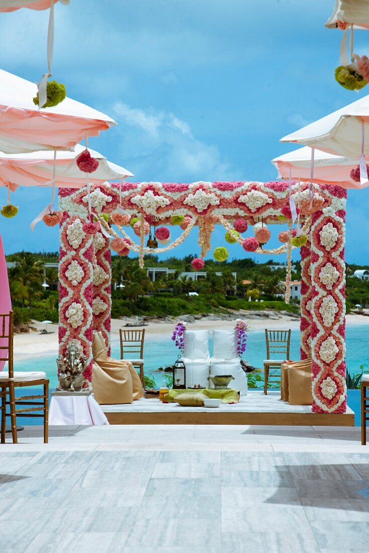 Indisches Hochzeitsfest im Freien auf einer Bühne, mit Blumen dekorierte Rahmen und Stühle mit weisser Husse für das Brautpaar, im Hintergrund Meeresküste