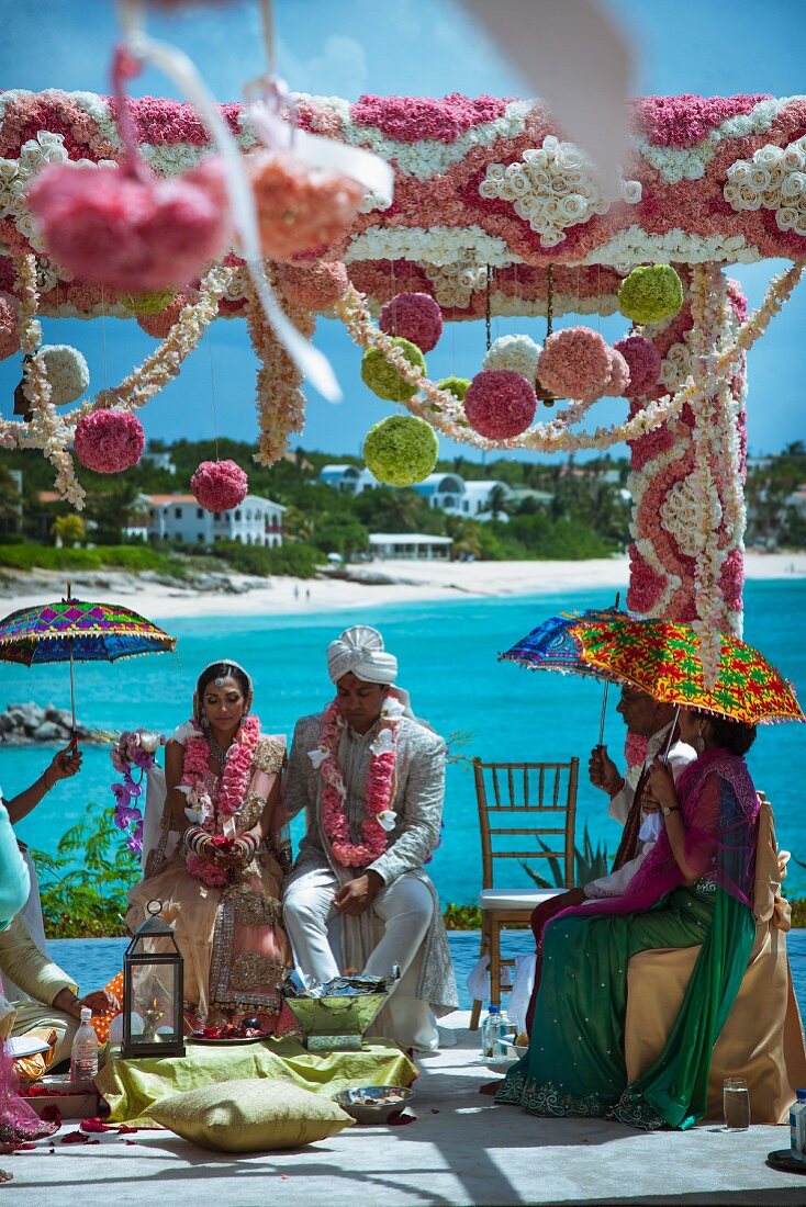 Indische Hochzeitszeremonie unter blauem Himmel am Strand mit üppigem romantischem Blumenschmuck