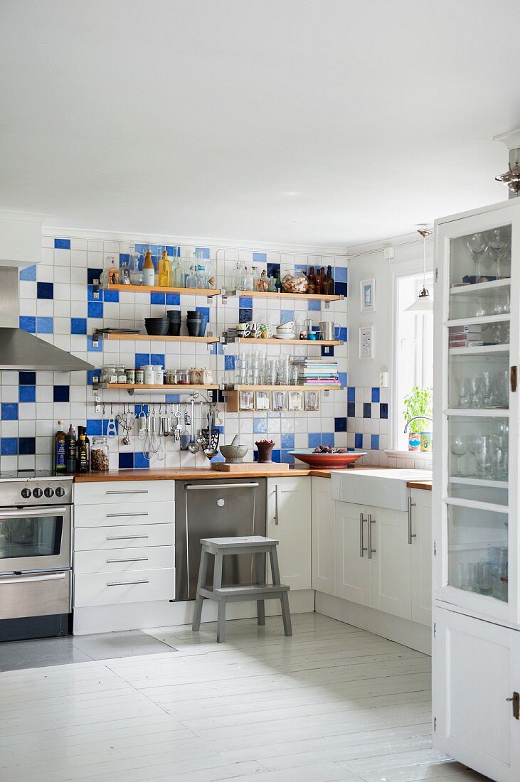 Küchenecke mit Regalbrettern an weiss-blau gefliester Wand über Küchenzeile mit weissen Unterschränken