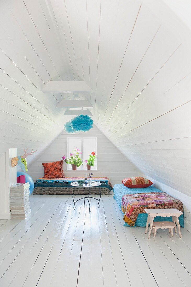 White wood-clad walls, ceiling and floor and colourful throws on couches in converted attic