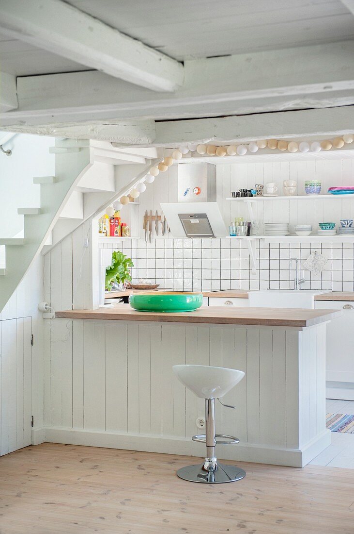 Bar stool at counter with white wood-clad base unit in open-plan kitchen