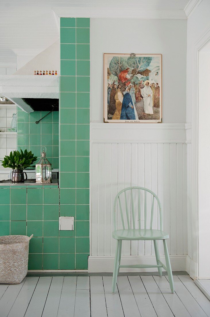 Pastel-green chair against white wood cladding next to green-tiled cooking area in Scandinavian kitchen