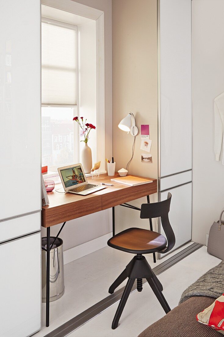 Drehbarer Bürostuhl aus Holz vor minimalistischem Schreibtisch am Fenster