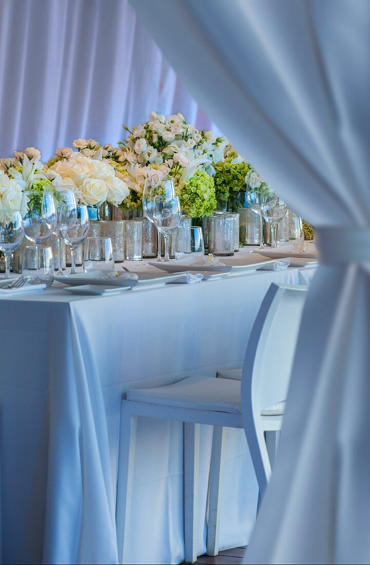 Festlich dekorierter Hochzeitstisch mit Blumensträussen in Reihe und Gedecke