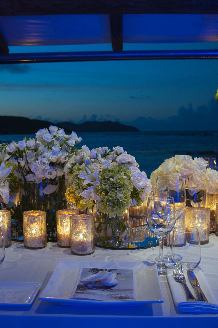 Windlichter und Blumensträusse auf festlich gedecktem Hochzeitstisch in Abendstimmung