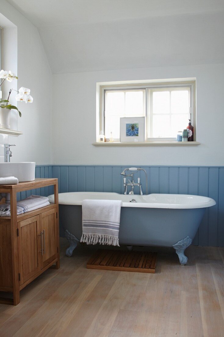 Freistehende hellblaue Badewanne vor passender Holzverkleidung mit nostagischem Flair