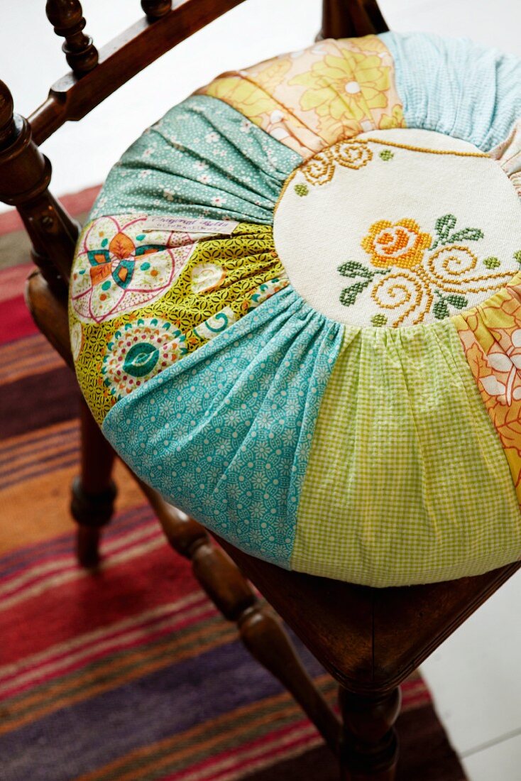 Turquoise and orange round patchwork cushion with embroidered panels on antique wooden chair