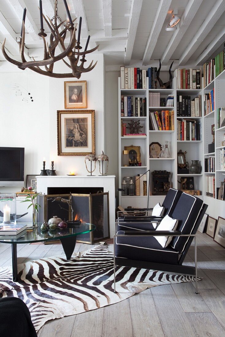 Black armchairs, classic coffee table and zebra-skin rug in front of fireplace in eclectic interior