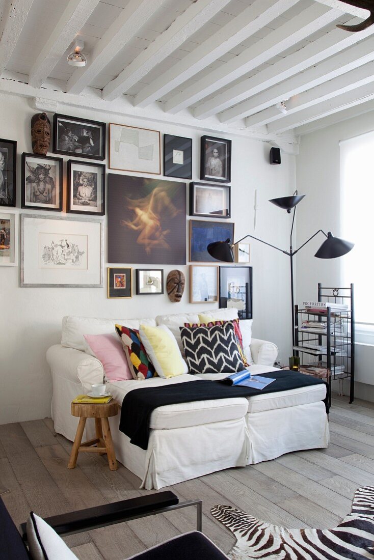 Multicoloured scatter cushions on white sofa and classic cantilever standard lamp in front of gallery of artworks