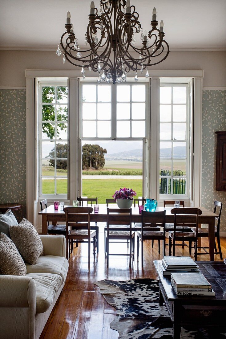Sofa and coffee table in front of dining area in elegant interior with view of landscape through French windows