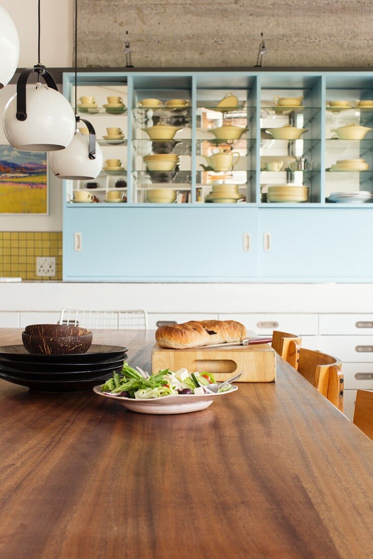 Blick vom Esstisch aus Holz auf ein Küchenregal mit gelbem Geschirr