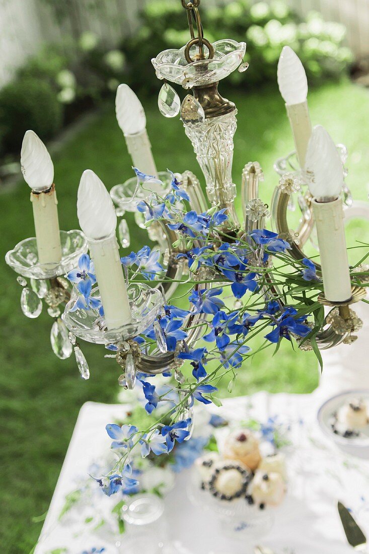 Crystal chandelier decorated with delphiniums hung over coffee table in garden