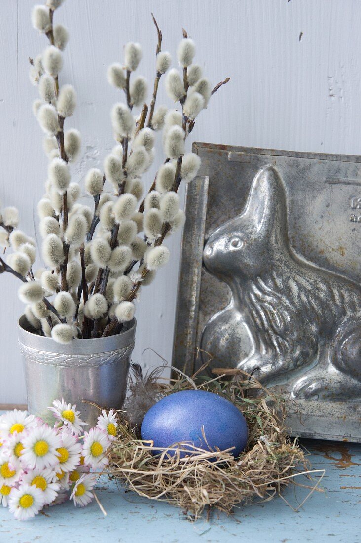 Easter still-life arrangement with willow catkins, daisies and Easter bunny cake tin