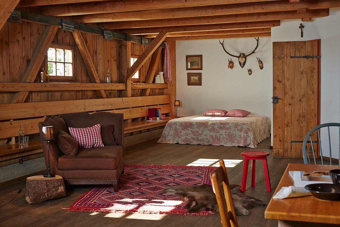 Offener Wohnraum mit Sitzmöbeln und Doppelbett in ländlichem Holzhaus