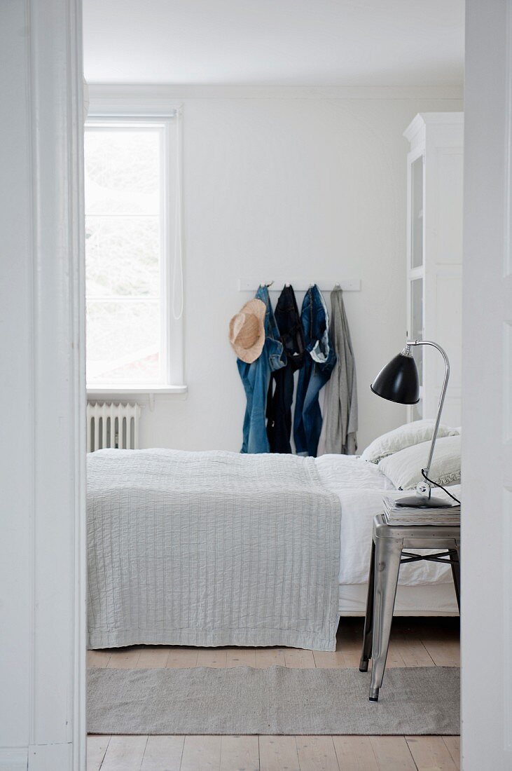 Weißes Schlafzimmer mit Jeanshosen an einer Hakenleiste