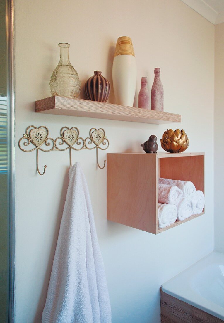 Handtuch auf Wandhakenleiste neben Regalbox mit Handtuchrollen, oberhalb Vasensammlung auf Wandkonsole