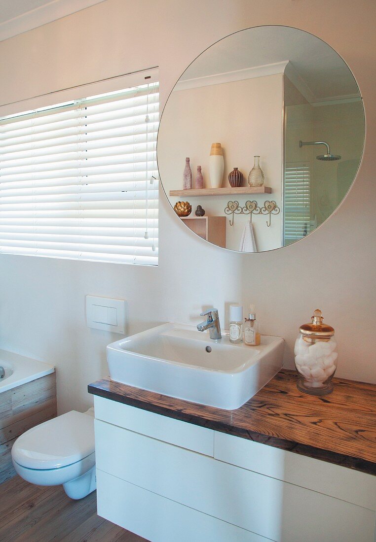 Washstand with white base unit and wooden top below round mirror