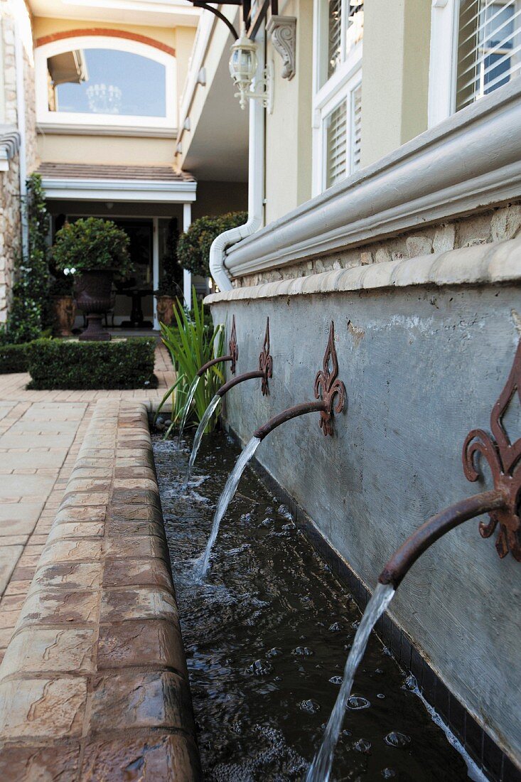 Vintage-style water spouts and stream running along façade of elegant country house