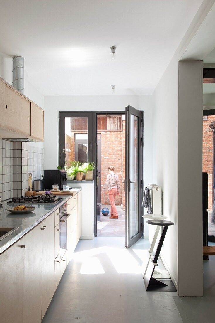 Einbauküche mit Designer-Barhockern und Blick durch geöffnete Fenstertür auf Backsteinfassade