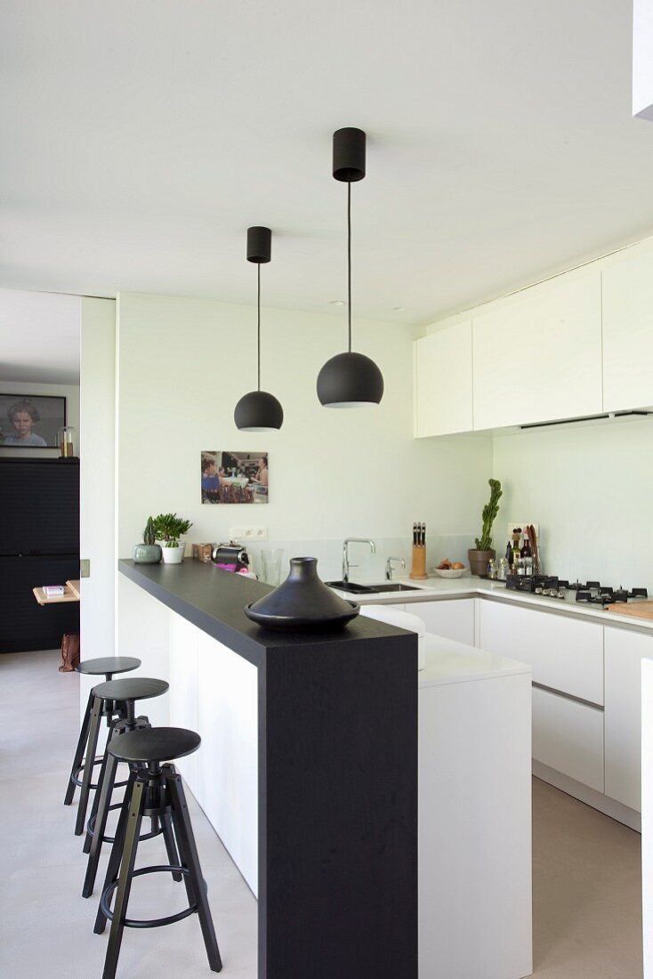 weiße Einbauküche mit schwarzer Küchentheke, passenden Pendelleuchten und Barhockern