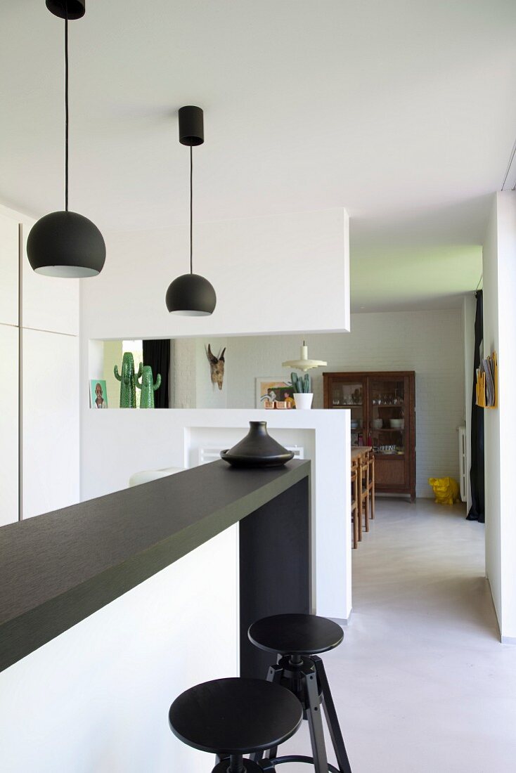 weiße Einbauküche mit schwarzer Küchentheke, passenden Pendelleuchten und Barhockern, Durchgang in Wohnbereich