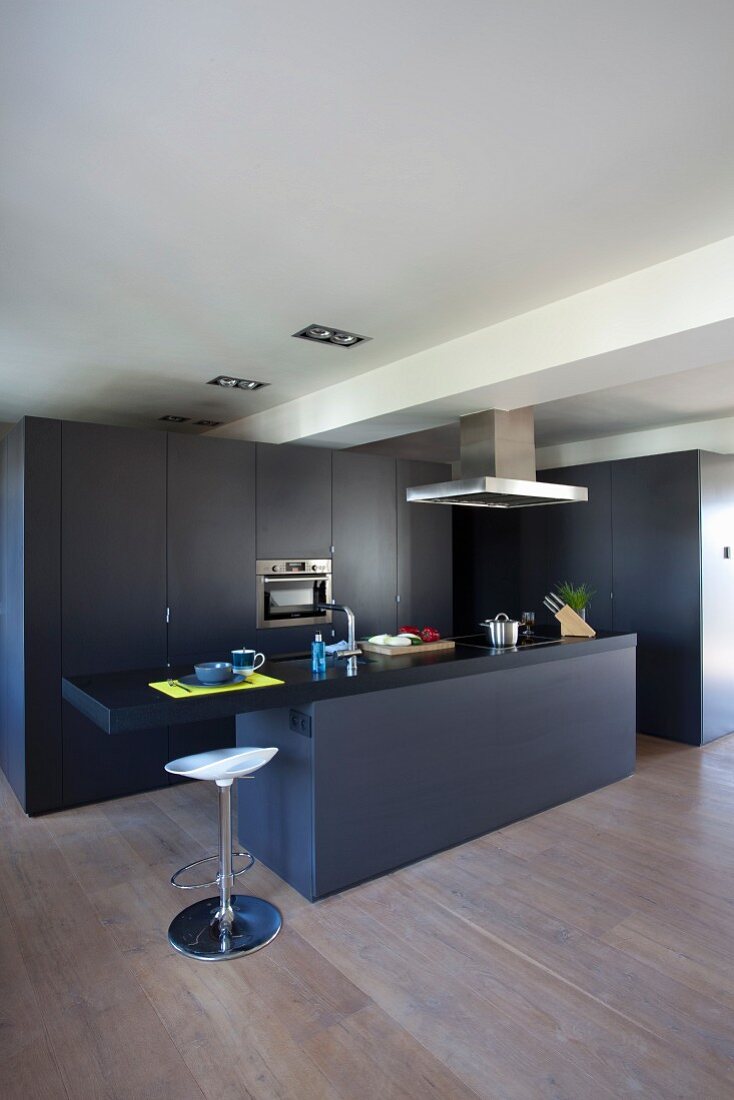 Black, floor-to-ceiling fitted kitchen cupboards, matching counter and white designer bar stool