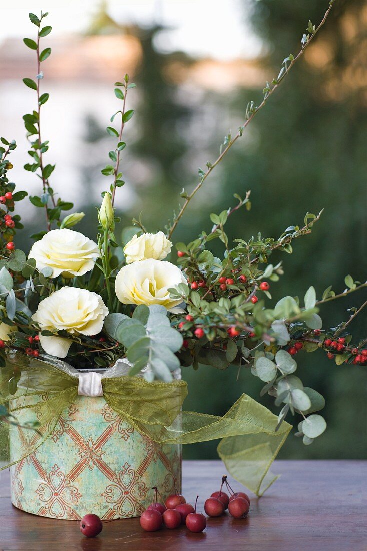 Herbstarrangement aus Zwergmispel, weißer Japanrose und Zieräpfeln in einer Dose mit Ornamenten