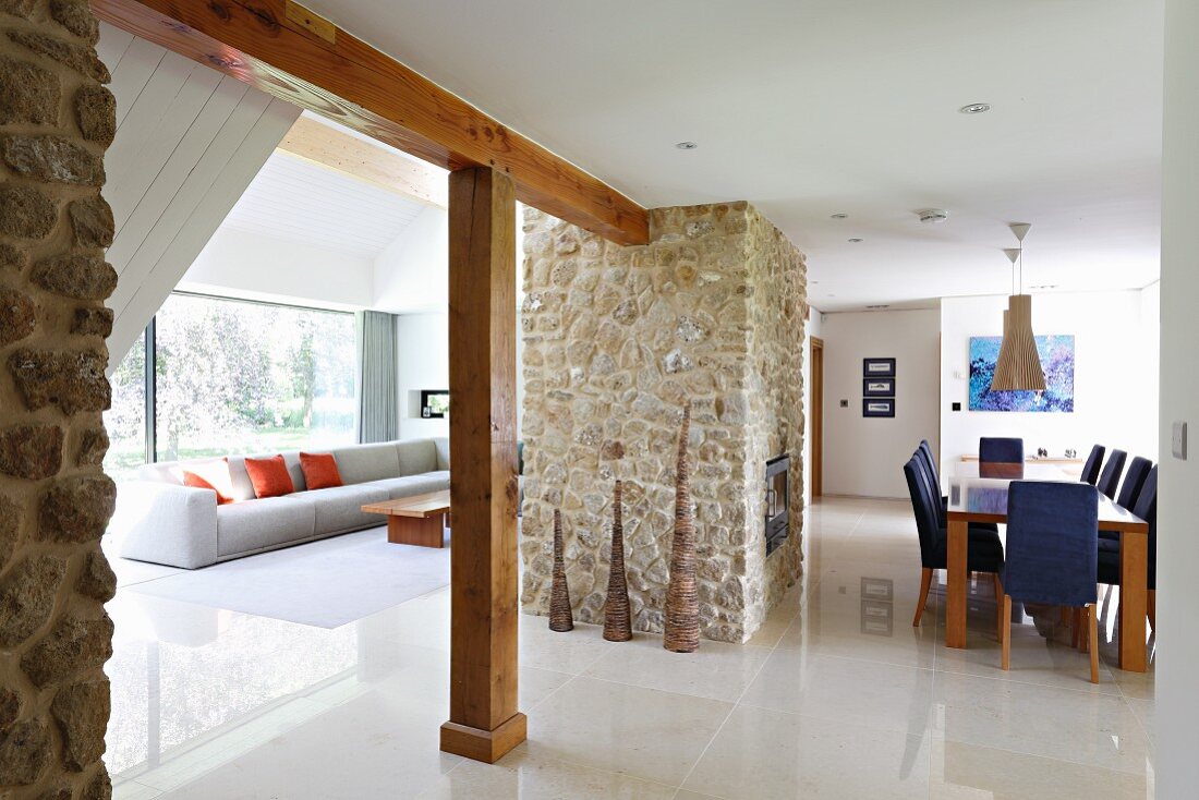 Offener Wohnraum mit hellem, poliertem Steinboden, Loungebereich und Essplatz, zentraler Natursteinblock mit Kamin
