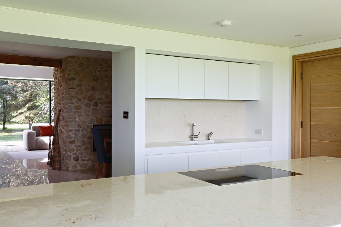 Narrow white fitted kitchen and open doorway leading into living room with stone chimney breast