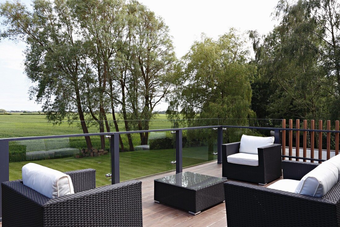 Outdoormöbel aus schwarzem Rattan mit weissen Polstern auf Terrasse vor Landschaft