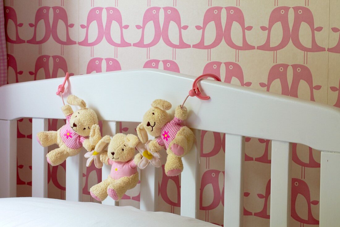 Garland of teddy bears on white cot against bird-patterned wallpaper