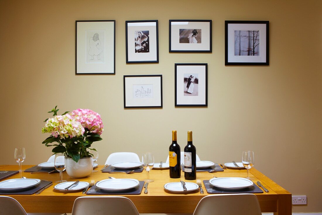 Wine bottles and hydrangea on set dining table in front of framed pictures on pastel wall