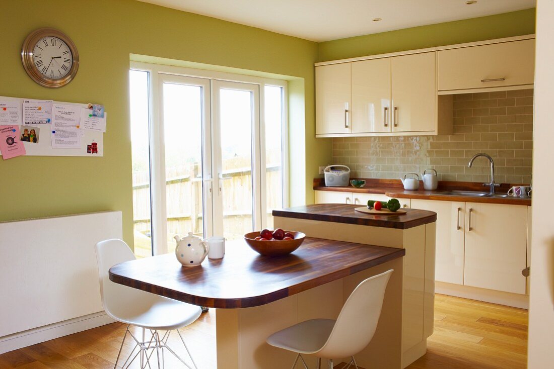 White classic shell chairs at table with wooden top abutting island counter in kitchen with green-painted walls