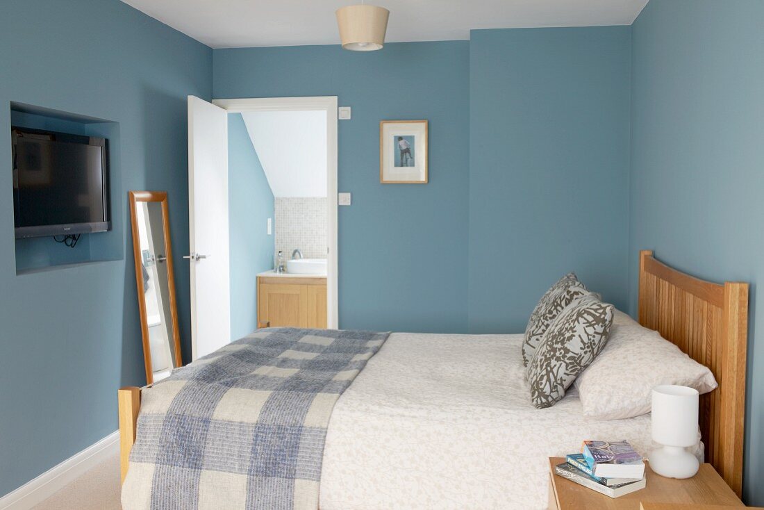 Doppelbett mit Holzkopfteil im Schlafzimmer mit blauen Wänden, im Hintergrund Badezimmer