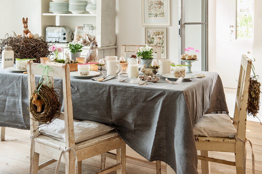 Graue Tischdecke auf gedecktem Oster-Frühstückstisch mit Vintage-Stühlen und Dekokränzen