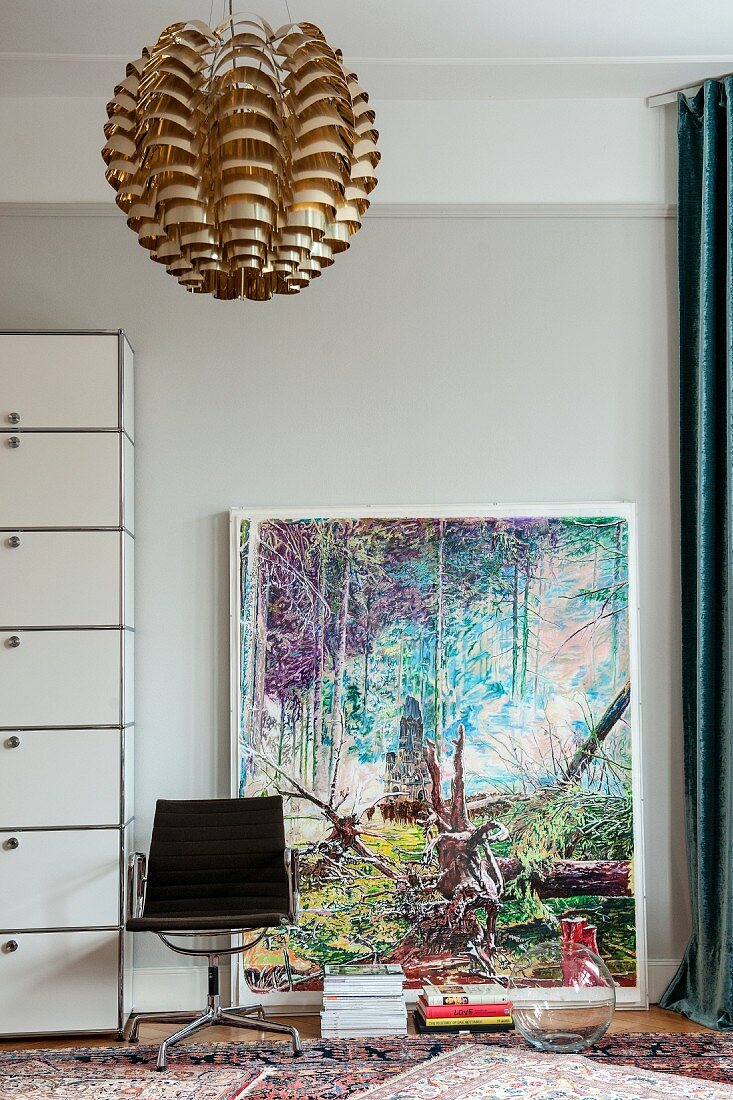 Modern artwork leant against pale grey wall behind vintage swivel chair and metallic pendant lamp