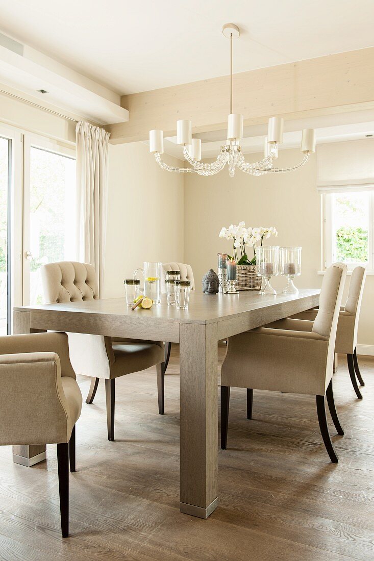 Elegant upholstered chairs around solid-wood table below chandelier in dining room in shades of cream
