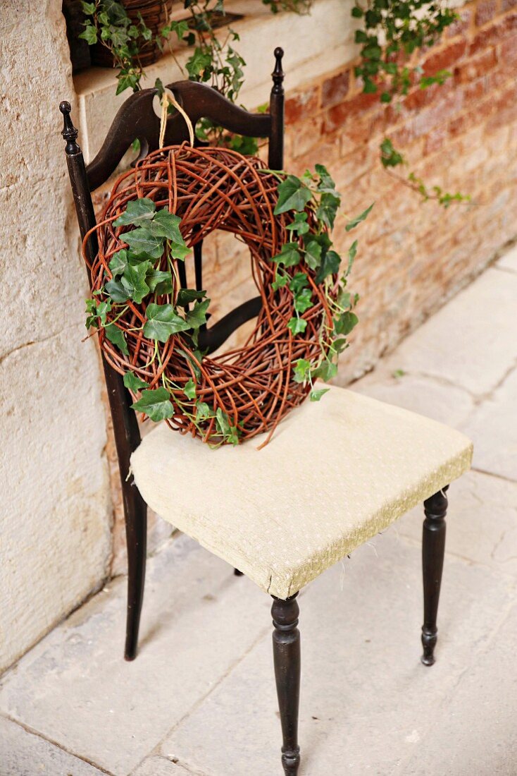 Wreath of wicker and ivy on chair against brick wall