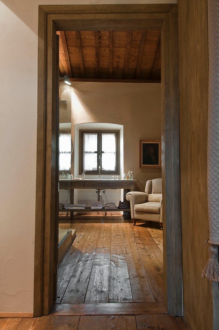 Blick durch offene Tür ins Bad auf Waschtisch am Fenster, rustikaler Dielenboden