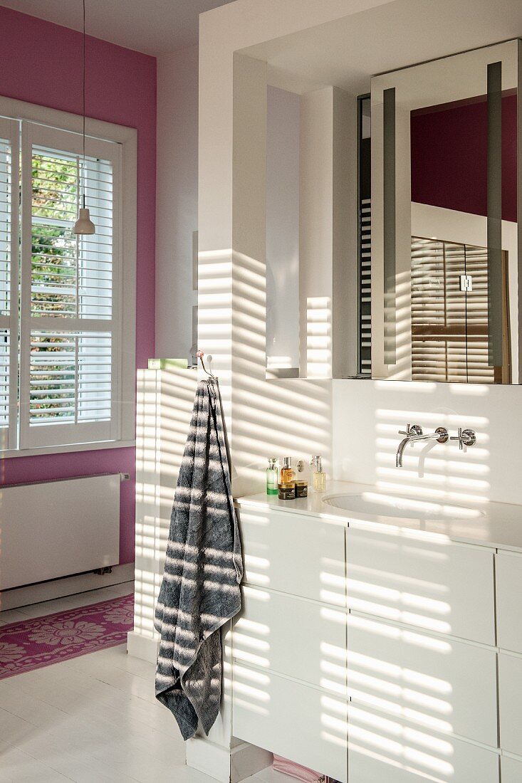 Pattern of light and shade on washstand with white base unit and wall-mounted tap below mirror in niche