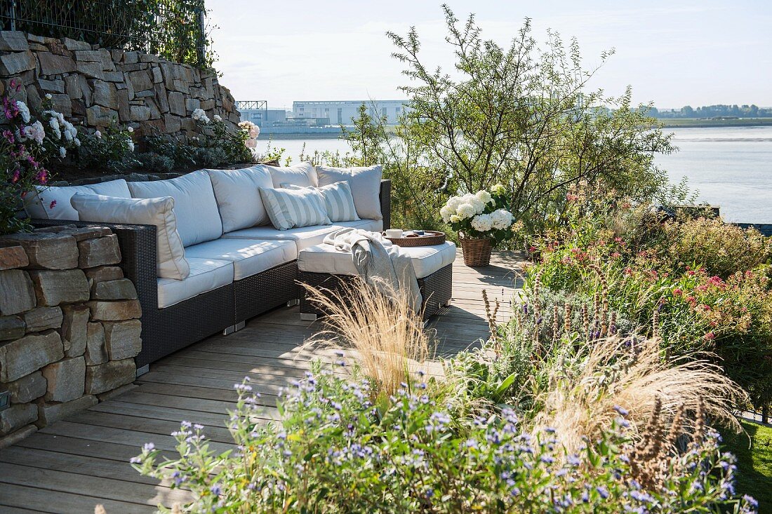Modernes Outdoor-Sofa mit hellen Polstern auf sonnenbeschienem Terrassenplatz mit Blick auf die Elbe