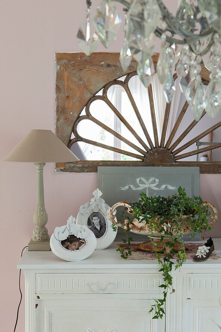 Arrangement of vintage-style ornaments, cardboard picture frame, table lamp and planted urn on top of cabinet