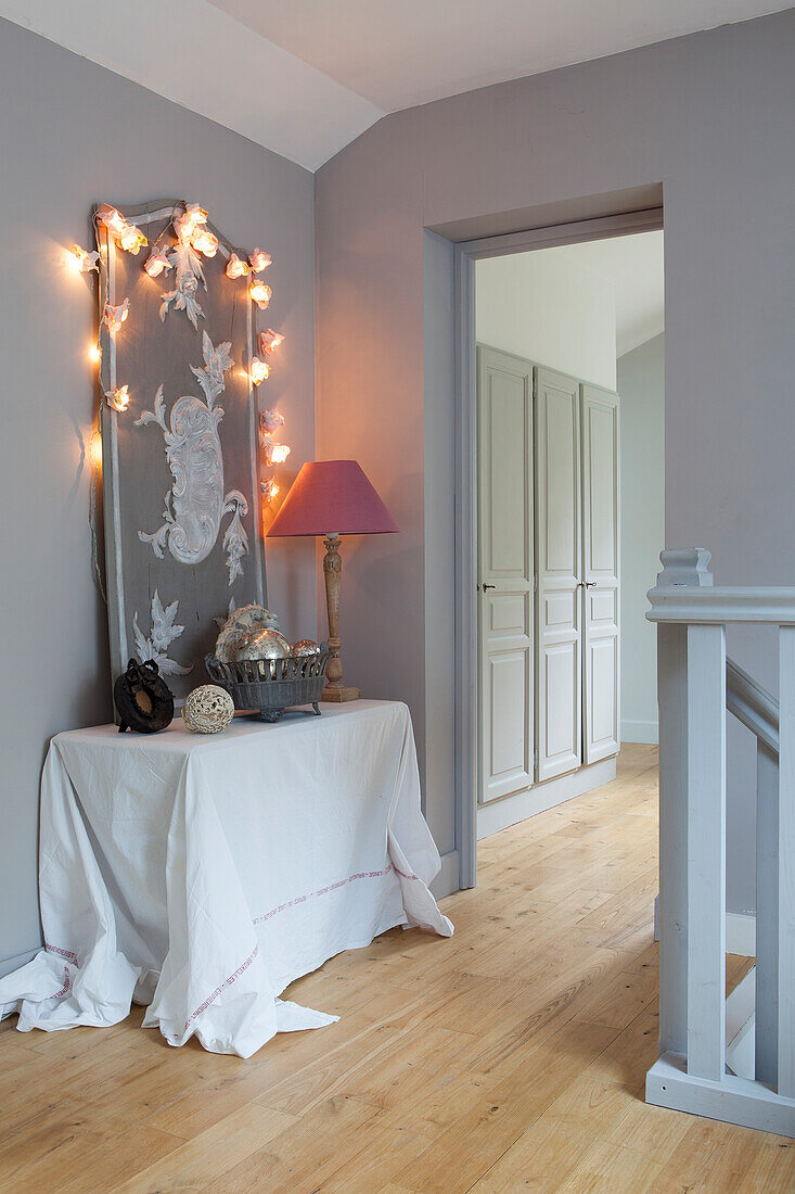 Panel decorated with fairy lights on top of console table with white tablecloth next to open doorway in stairwell