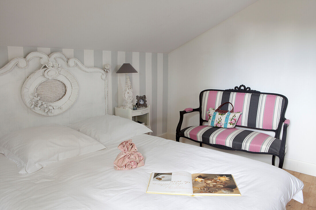 Double bed with curved headboard beside couch with grey and pink striped upholstered under sloping ceiling